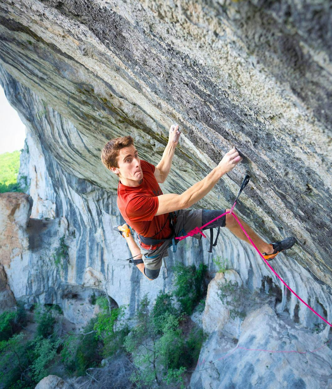 Ein Kletterer in mitten einer Steilen Wand von oben fotografiert: Er ist mit einem Seil gesichert das nach unten verläuft. Er versucht gerade nach oben zu klettern. Die Beine sind weit auseinander im Fels gespreizt. Die Kraftanstrengung ist ihm im Gesicht anzusehen das etwas Schmerzverzerrt ist. © ┬®_Reel Rock - DNA_Sébastien Bouin